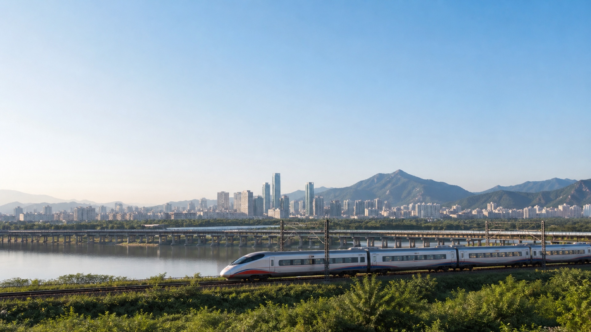Modern high-speed train crossing a river near a Korean city and mountains